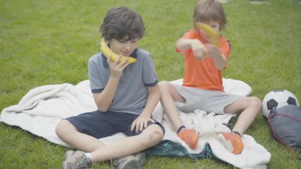 Portrait de drôles de petits garçons gais utilisant des bananes comme téléphones et se battant avec des fruits. Sans soucis amis caucasiens s'amuser à l'extérieur. Concept repos et loisirs. — Video