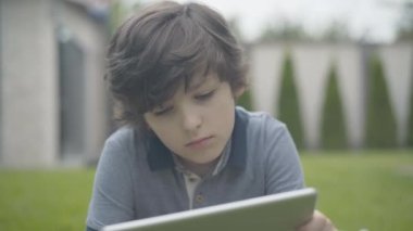 Dışarıda tablet kullanan yalnız çocuğun yakın plan portresi. Kafkasyalı mutsuz öğrenci hafta sonlarını evde yalnız geçiriyor. İnternette sörf ya da oyun oynayan üzgün çocuk..