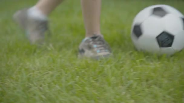 Camera live urmărește picioarele băiețelului caucazian în adidași care rulează mingea de fotbal în aer liber. Copil de nerecunoscut joc de sport pe gazon verde. Sport și stil de viață sănătos . — Videoclip de stoc