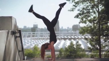 Güçlü, genç, sıska bir kadın elleri ve ayakları üzerinde duruyor. Beyaz kadın sporcu ya da jimnastikçi, gün doğumunda arka planda şehirle birlikte açık havada antrenman yaparken geniş açıda görülüyor..