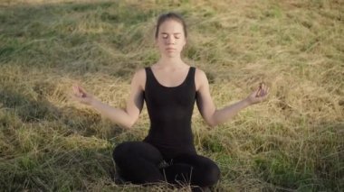 Yoga nilüferinde oturan güzel, kendine güvenen beyaz kadın portresi açık havada güneş ışığında poz veriyor. Genç bayan yogi güneşli yaz gününde çayırda egzersiz yapıyor. Huzur ve sükunet.