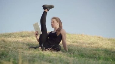Tepede bacağını kaldırmış ve tablet selfie makinesinin önünde konuşan sıska bir kadın. Çevrimiçi kablosuz sohbeti sabahları antrenman olarak kullanan esnek beyaz jimnastikçi..