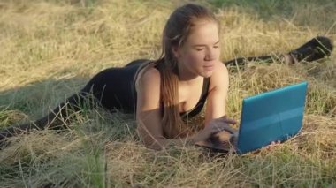 Gülümseyen genç sporcu bayana kamera yaklaşıyor. İnternette sörf yaparken çayırda ayrı poz vermek gibi. Kendine güvenen Kafkas jimnastikçinin portresi. Gün doğumunda dizüstü bilgisayar eğitimi almış..