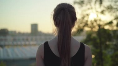 Güneşin batışında bulanık şehir parkına doğru yürüyen esmer kadın. Pozitif beyaz kadın akşam güneşinde dışarıda geziniyor..