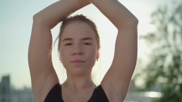 Close-up portret van jonge charmante blanke vrouw die handen opsteekt en glimlacht naar de camera in het zonlicht. Mooie brunette turner poseren in zonnestralen buiten. — Stockvideo