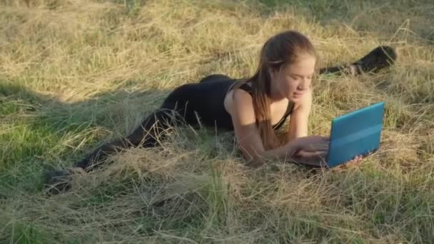 젊은 여자 체조 선수가 분리되어 앉아서 노트북을 사용하고 있습니다. 갈색 갈색의 유연 한 카프카스 여성이 일출 때 온라인으로 인터넷 서핑을 하거나 문자 메시지를 보내는 모습. 햇빛을 받는 행복 한 스포츠맨. — 비디오