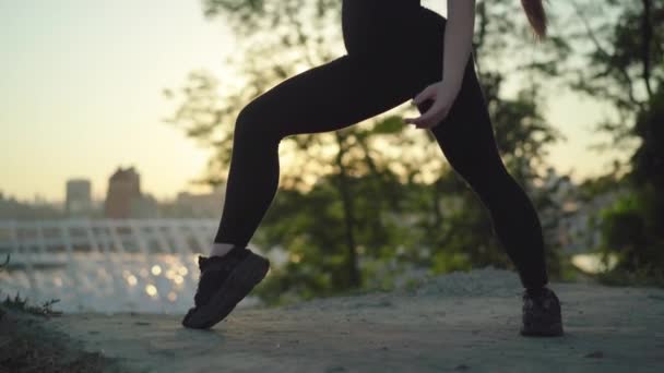Camera beweegt langs prachtige slanke lichaam van jonge blanke sportvrouw training bij zonsondergang buiten. Side view portret van charmante vrouwelijke yogi oefenen in zonnestralen met stedelijke stad op de achtergrond. — Stockvideo
