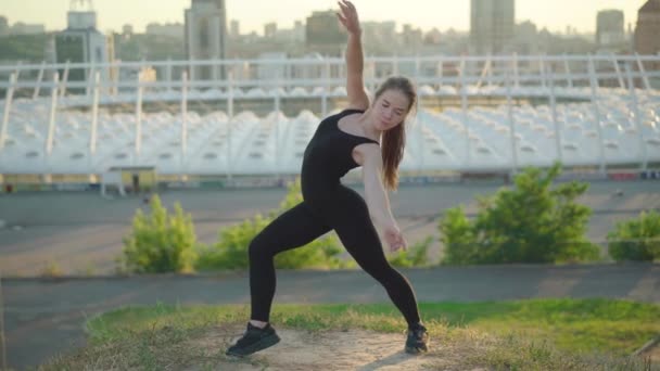 Pohled zezadu na štíhlou mladou ženu na pozadí města. Široký záběr sebevědomí krásné kavkazské gymnastky cvičení venku na slunné letní den. — Stock video