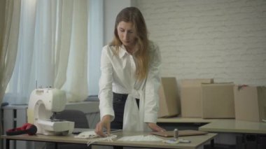 Yoğunlaştırılmış terzi portresi Covid yüz maskeleri dikmek için bir fikir edindi. Dikiş makinesi olan ve gülümseyen genç, düşünceli, beyaz bir kadın. Coronavirus iş hayatı tarzı.