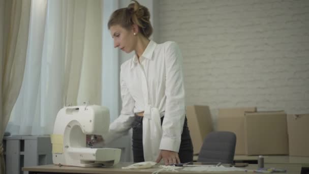 Confused Caucasian seamstress looking at broken sewing machine in atelier. Middle shot portrait of embarrassed young woman working in workshop. Clothing design and occupation. — Stock Video