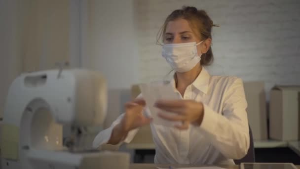 Portret van zelfverzekerde naaister naaien Covid-19 gezicht maskers tijdens coronavirus wereldwijde pandemie. Jonge blanke vrouw werkt in atelier met naaimachine. — Stockvideo