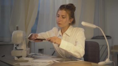 Konsantre genç terzi Covid-19 'un yüz maskesinin fotoğrafını çekiyor. Küresel virüs salgını sırasında kendine güvenen beyaz kadın koronavirüs koruyucu yüz örtüsü satıyor..