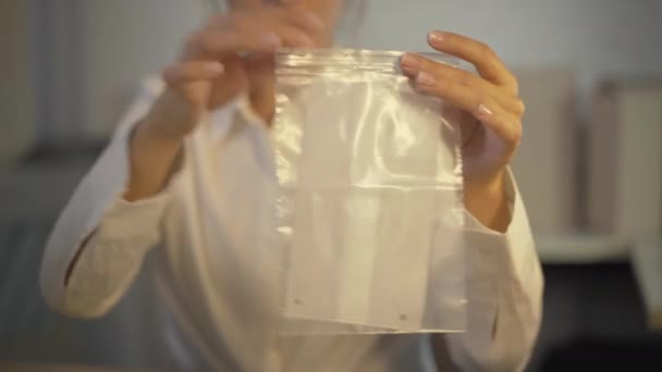 Embalaje de sastre joven irreconocible Covid-19 máscara facial y cuerdas en paquete de plástico transparente. Costurera caucásica haciendo cubiertas protectoras de la cara del paño para la venta durante la pandemia del coronavirus. — Vídeos de Stock