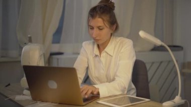 Kendine güvenen beyaz kadın terzinin portresi klavyede daktilo, dizüstü bilgisayarı kapatma ve zafer jesti yapma. İnternet sitesi üzerinden elbise satan başarılı bir terzi..