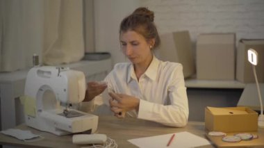 Atölyede ya da evde koronavirüs maskesi dikerken gergin bir kadın. Dikiş makinesine vurup düşünen genç beyaz kadın portresi. Covid-19 salgını sırasında aşırı çalışma ve stres.