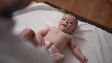 Neşeli bir bebek, yumuşak ve rahat bir yüzeyde bebek bezi değiştirirken keyifli anlar yaşar ve eğlenir.