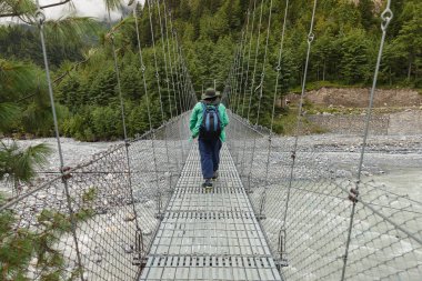 Bir trekker arkadan görünüm üzerindeki Nepal'deki bir asma köprü.