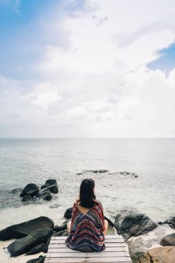 Köprüde oturan ve denize bakan kadının arka görünümü.