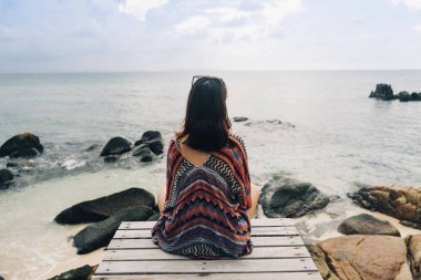 Köprüde oturan ve denize bakan kadının arka görünümü.