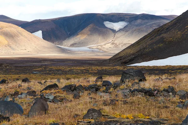 Volcanic landscape with black rocks and earth and poor vegetation in autumn, Kamchatka peninsula, Russia. The Earth befor the beginning of time, panoramic view on the harsh valley an snowy mountains in heart shaped.