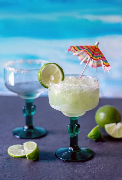 cold and icy frozen margarita drinks with slices of lime  and an umbrella