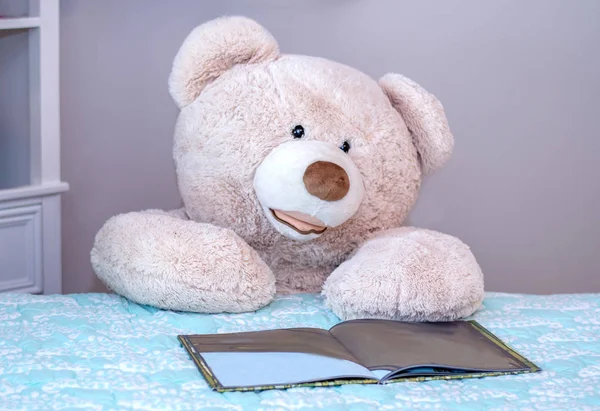 Big teddy bear kneels beside the bed and reads a child's picture book