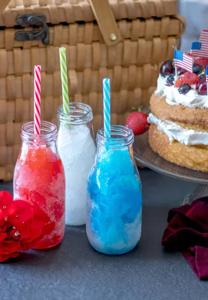 Dessert and drinks for your 4th of july celebration.  fresh strawberry angel food cake with blueberries, strawberries, cherries and whipped cream, and colorful frozen drinks with or without alcohol