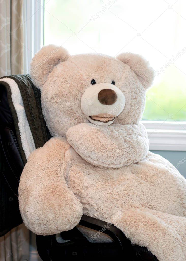 This very large teddy bear sits in a full size chair and points off into the distance; he went that way! he says
