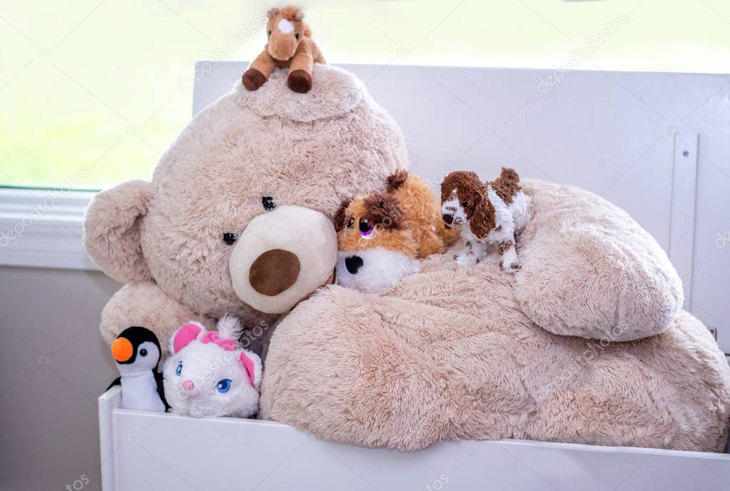 A large stuffed bear is covered with many smaller stuffed toys, a toy friendship in the playroom