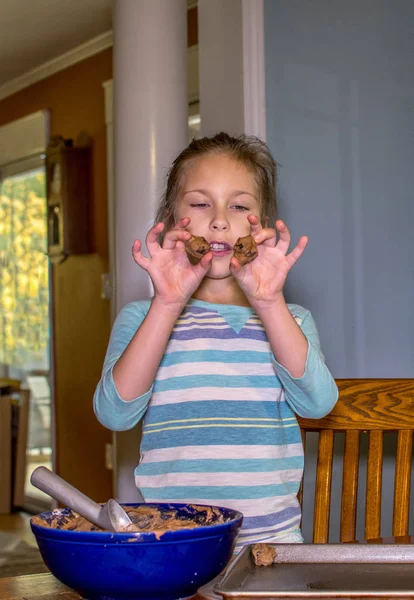 A little girl shows off the cookie dough balls she has formed for chocolate chip cookies