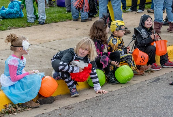 2018年10月27日一排孩子们穿着有趣的万圣节服装 坐在路边等待活动开始 — 图库照片
