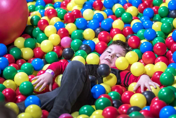 Мальчик лежит в большой куче разноцветных шаров — стоковое фото