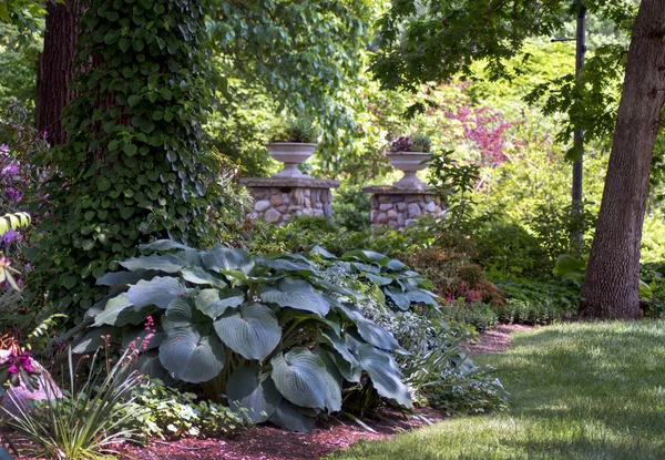 Pilares de piedra sostienen macetas de flores en un bonito jardín — Foto de Stock