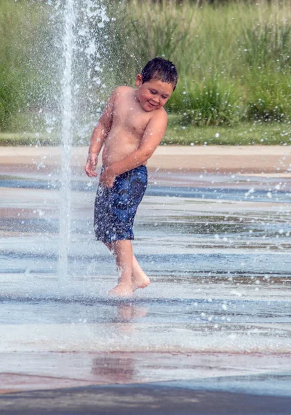 Fröhlicher Junge spielt in einem Springbrunnen-Planschbecken — Stockfoto