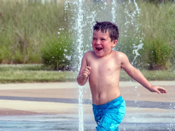 Rire garçon cours à travers une fontaine d'eau — Photo