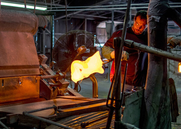 стеклянный рабочий перелистывая расплавленное горячее стекло, чтобы сделать витражи
