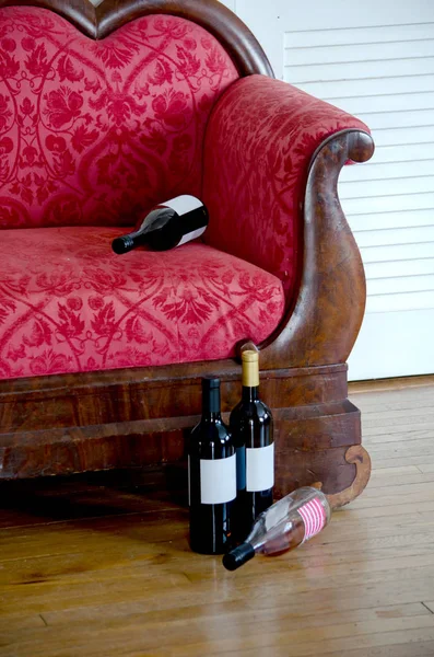 Garrafas de vinho vazias por um sofá antigo — Fotografia de Stock