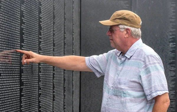 Older man finds the name of a friend on the wall — Stock Photo, Image