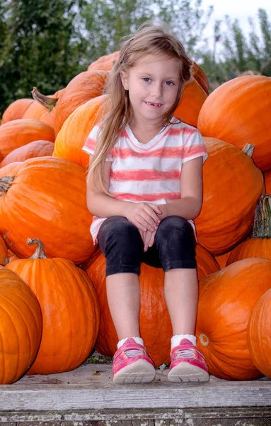 Klein meisje met een stapel pompoenen — Stockfoto
