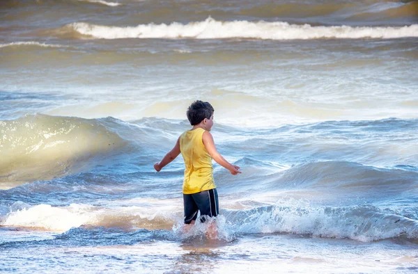 一个小男孩似乎指挥着波浪在密歇根湖的一个活跃的海滩上升起 — 图库照片