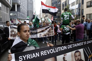 8 Eylül 2018'de Belçika'nın başkenti Brüksel'de Suriye Devlet Başkanı Beşar Esad'a karşı düzenlenen protestoda suriye bayrakları sallayıp slogan atan insanlar.