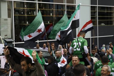 8 Eylül 2018'de Belçika'nın başkenti Brüksel'de Suriye Devlet Başkanı Beşar Esad'a karşı düzenlenen protestoda suriye bayrakları sallayıp slogan atan insanlar.