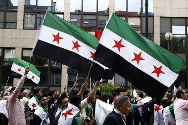 8 Eylül 2018'de Belçika'nın başkenti Brüksel'de Suriye Devlet Başkanı Beşar Esad'a karşı düzenlenen protestoda suriye bayrakları sallayıp slogan atan insanlar.