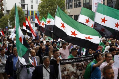 8 Eylül 2018'de Belçika'nın başkenti Brüksel'de Suriye Devlet Başkanı Beşar Esad'a karşı düzenlenen protestoda suriye bayrakları sallayıp slogan atan insanlar.