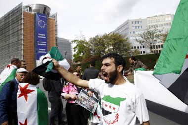 8 Eylül 2018'de Belçika'nın başkenti Brüksel'de Suriye Devlet Başkanı Beşar Esad'a karşı düzenlenen protestoda suriye bayrakları sallayıp slogan atan insanlar.