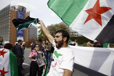 8 Eylül 2018'de Belçika'nın başkenti Brüksel'de Suriye Devlet Başkanı Beşar Esad'a karşı düzenlenen protestoda suriye bayrakları sallayıp slogan atan insanlar.