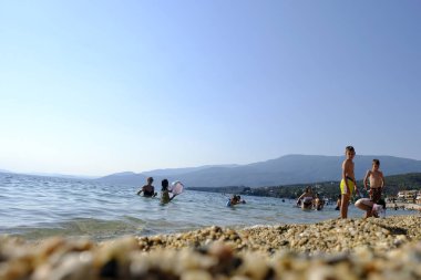 İnsanlar 6 Ağustos 2018'de Yunanistan'ın Afissos köyü sahilinde denizde yüzerken güneşli havanın tadını çıkarıyorlar.