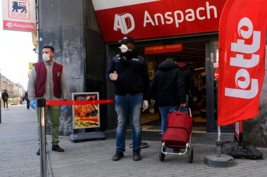 Brüksel, Belçika. 18 Mart 2020. Bir muhafız, Belçika hükümeti koronavirüs kilitlemesi uygulamadan önce süpermarketin girişini kontrol ediyor..