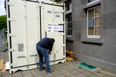  Belçika 'nın Brüksel kentindeki Verrewinkel Mezarlığı' nda 29 Nisan 2020 'de bir belediye çalışanı, içinde COVID-19 kurbanlarının tabutlarının bulunduğu soğutulmuş bir konteynırı açıyor.