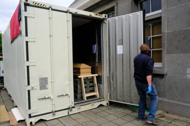  Belçika 'nın Brüksel kentindeki Verrewinkel Mezarlığı' nda 29 Nisan 2020 'de bir belediye çalışanı, içinde COVID-19 kurbanlarının tabutlarının bulunduğu soğutulmuş bir konteynırı açıyor.